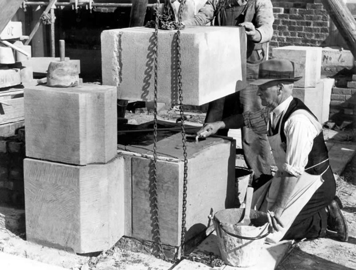 Photograph of a stonemason watching a block of stone being lowered into place