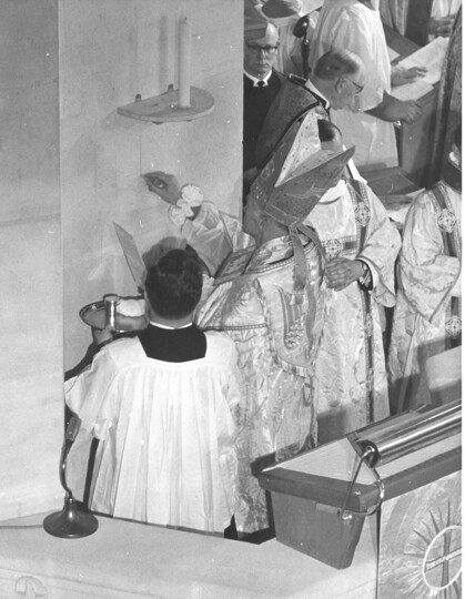 Photograph of the Bishop inscribing the Cross of Consecration on the wall above the Pulpit