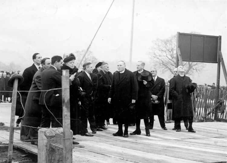 Photograph of Queen Mary pulling a rope, watched by a group of gentlemen